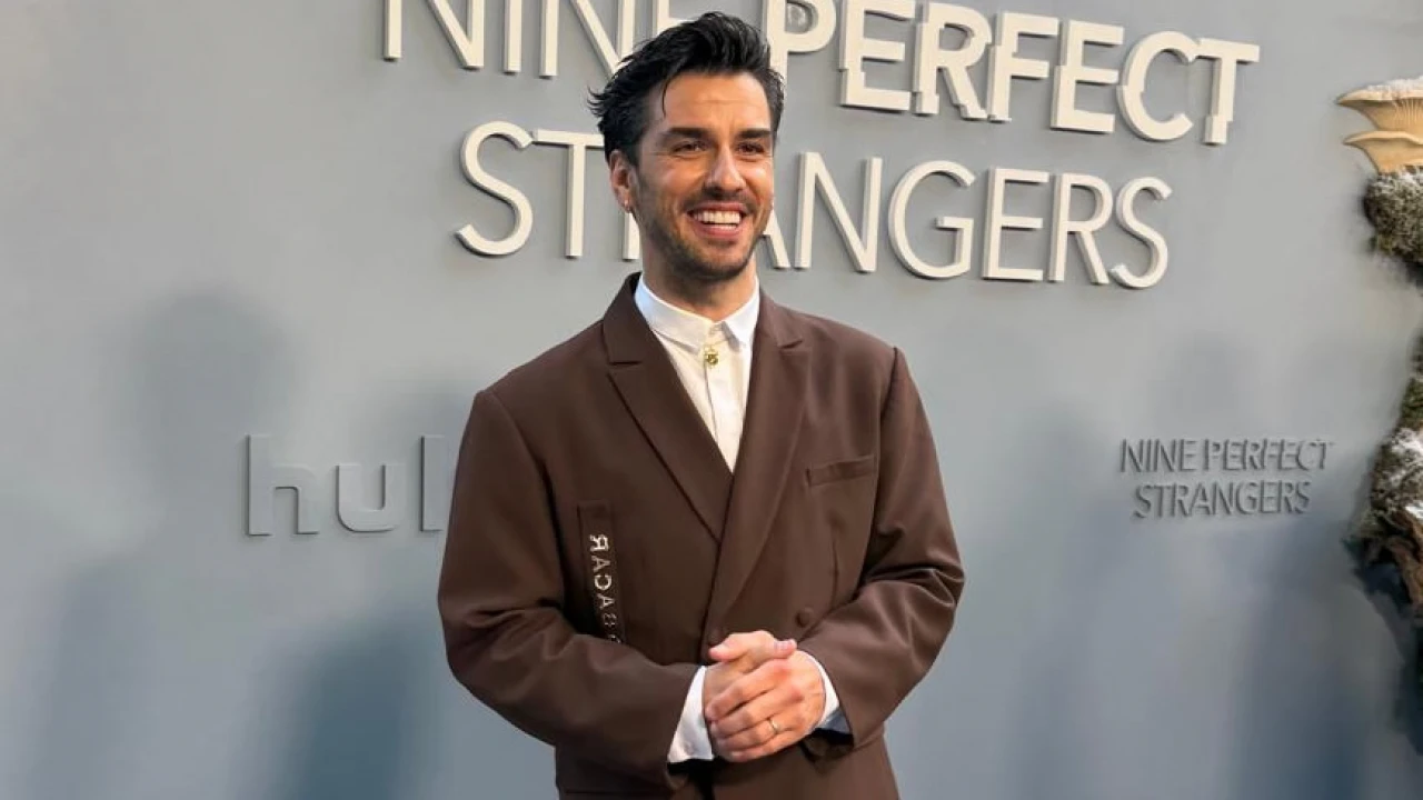 Aras Aydın, 'Nine Perfect Strangers' yazılı promosyon paneli önünde resmi pozunda. Kahverengi takım elbise ve beyaz gömlek giymiş, hafif gülümseyerek kameraya bakıyor. Ellerini önünde kavuşturmuş halde duruyor. Muhtemelen dizinin tanıtım etkinliğinden bir kare. Aras Aydın, 'Nine Perfect Strangers' yazılı promosyon paneli önünde resmi pozunda. Kahverengi takım elbise ve beyaz gömlek giymiş, hafif gülümseyerek kameraya bakıyor. Ellerini önünde kavuşturmuş halde duruyor. Muhtemelen dizinin tanıtım etkinliğinden bir kare.