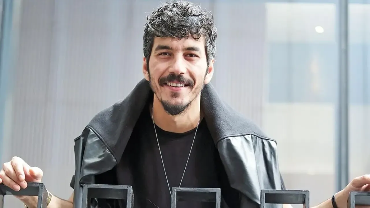 Mert Doğan gülümseyen pozunda — siyah deri yelek ve kolye ile set fotoğrafı